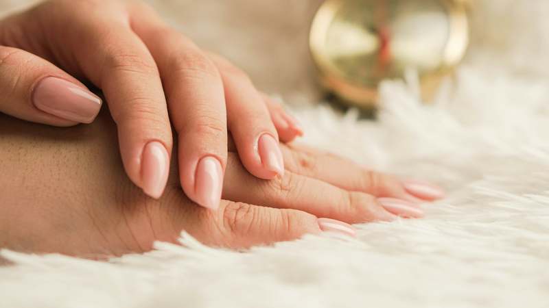 Close-up of strong, polished nails with glass-like shine beside natural nail care products including a clear nail strengthener bottle